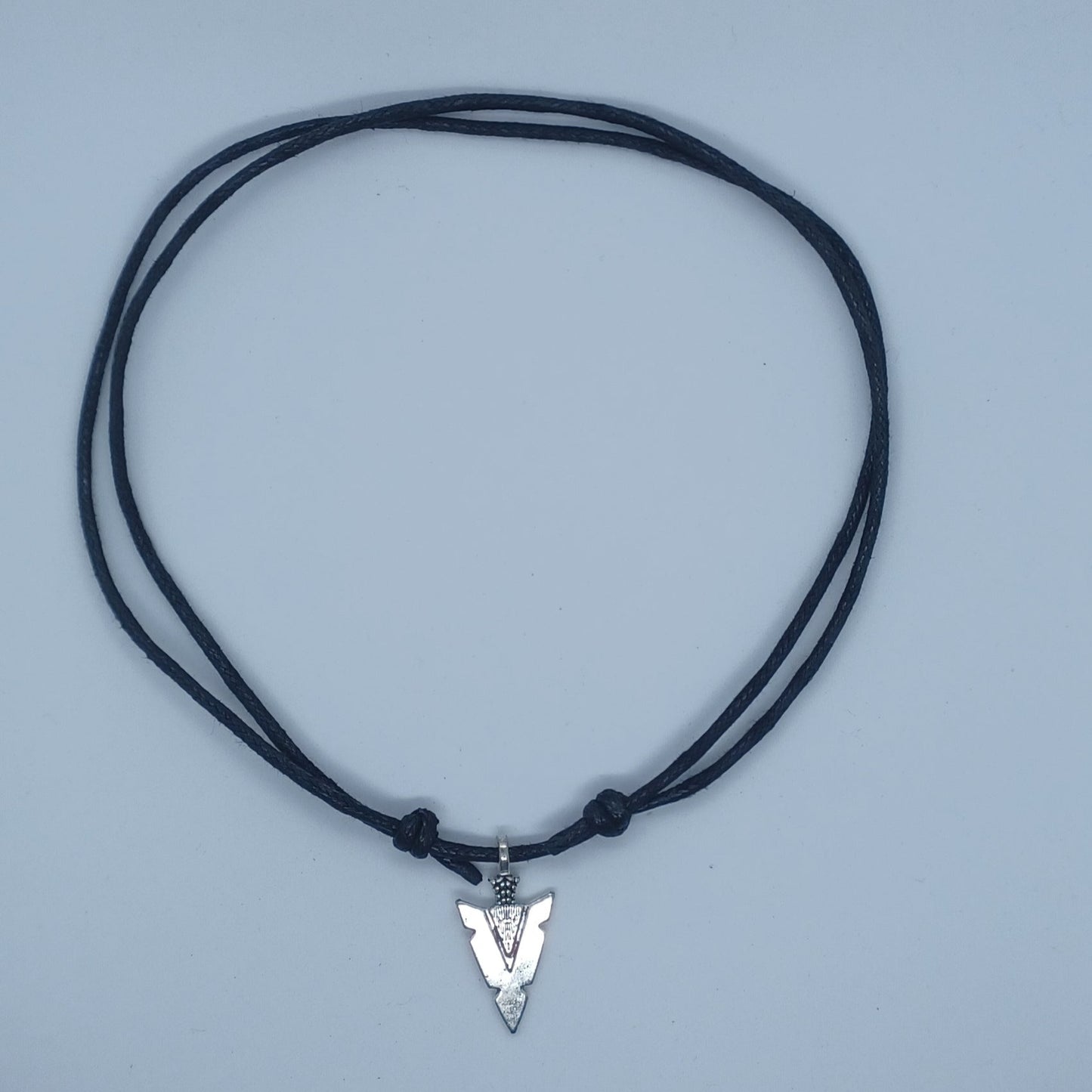 Unisex arrowhead sliding knot necklace shown at it's shortest length collar bone area. The necklace is black cotton cord 2mm thick and the arrowhead is made from Tibetan silver.